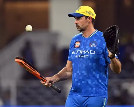 Stephen Fleming in a blue Chennai Super Kings shirt tosses a cricket ball while holding a bat and wearing a glove
